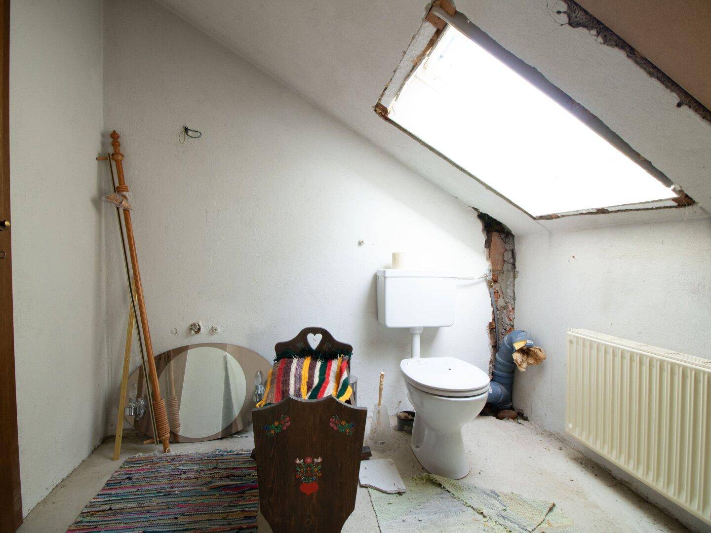 Badezimmer im Rohbauzustand mit Toilette und Dachfenster, unfertig.