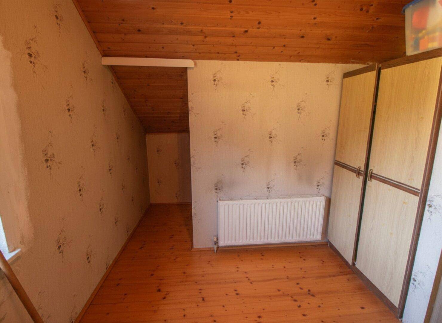 Schlafzimmer mit Holzboden und Heizkörper, Zugang zu einem weiteren Raum.