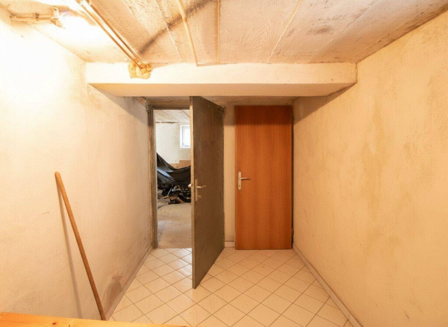 Kellerraum mit Fliesenboden und Holztür, funktionaler Abstellbereich.