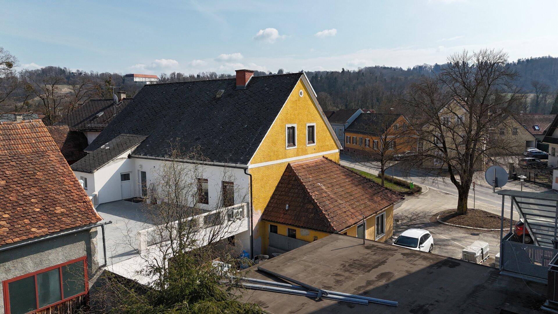 Gesamtansicht des Anwesens von hinten mit dem gelben Gebäude und der angrenzenden Terrasse.
