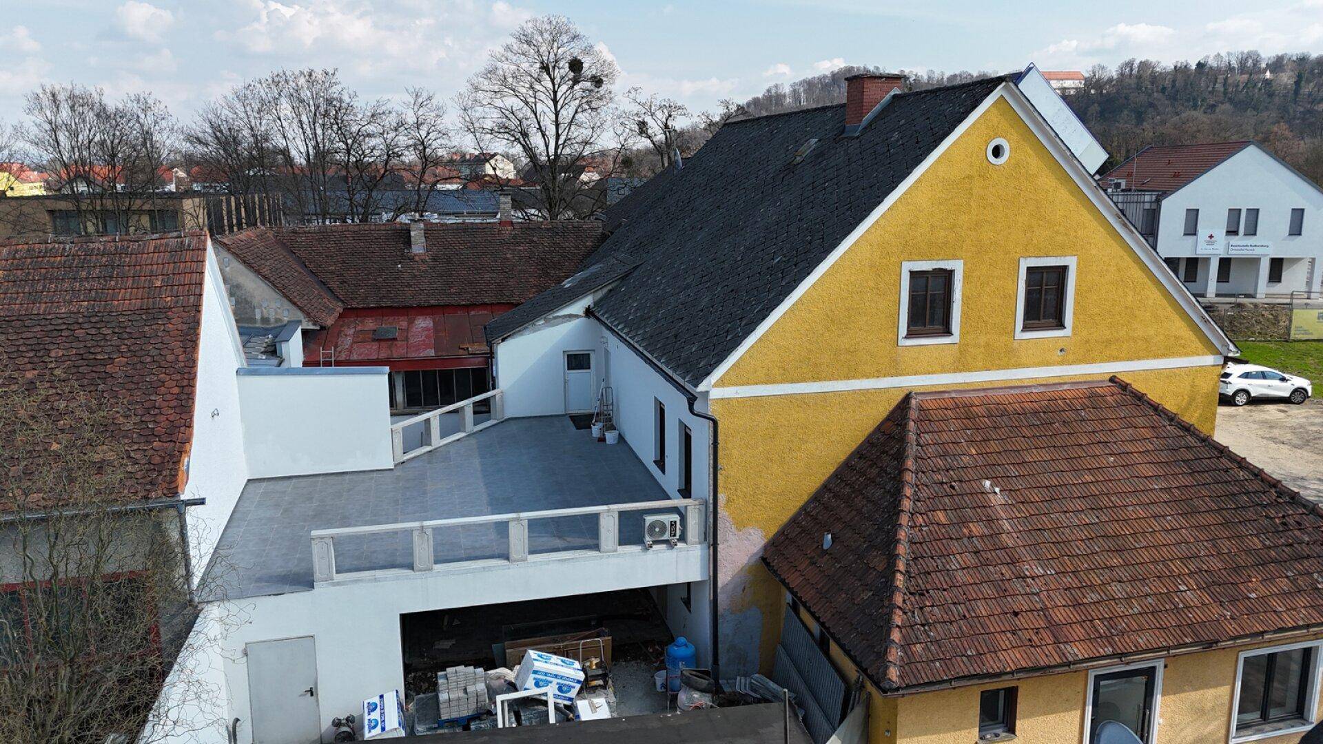 Rückansicht des Gebäudes mit einer großen, gefliesten Terrasse und dem gelben Hauptgebäude.