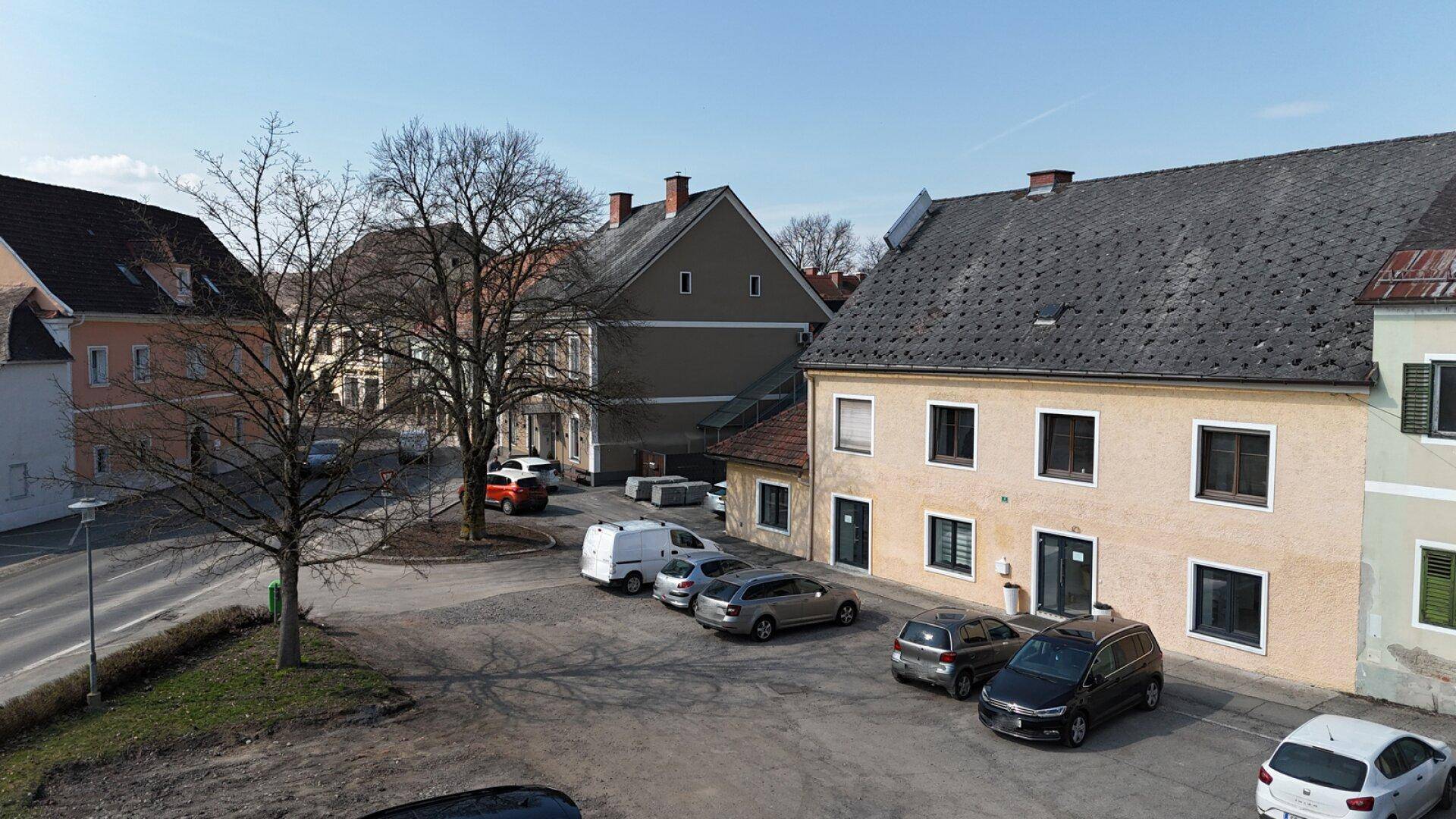 Vorderansicht des Gebäudes mit Parkplätzen und der umliegenden Bebauung an einem sonnigen Tag.
