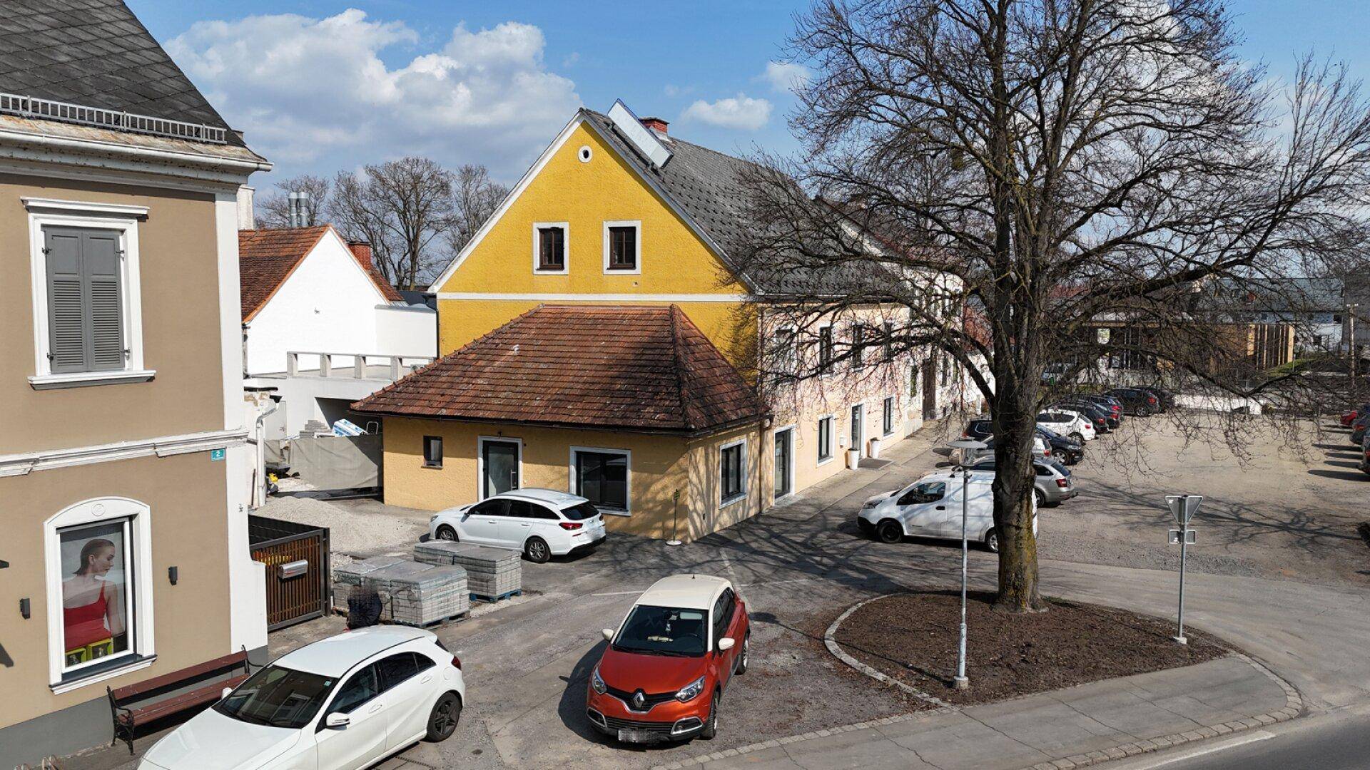 Ansicht des gelben Gebäudes mit braunem Dach und umliegenden Parkplätzen an einem sonnigen Tag.