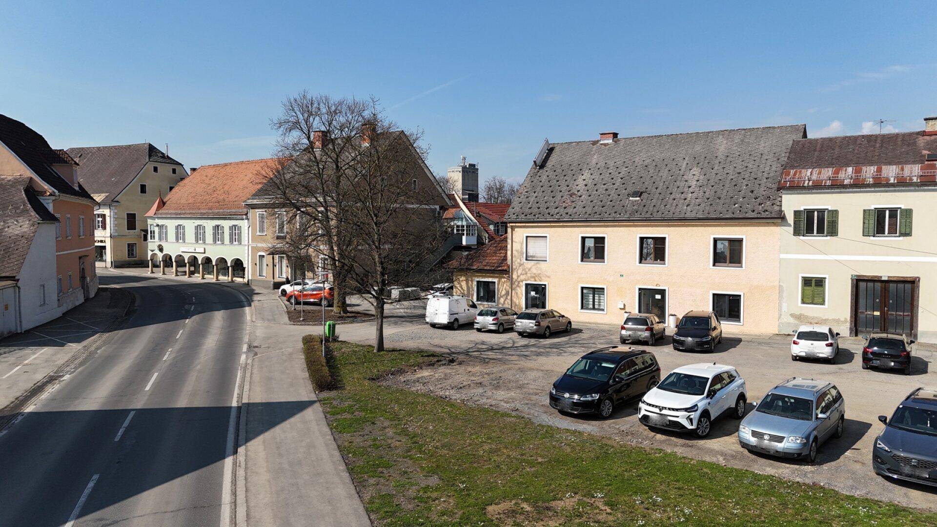 Blick auf die Straße, Parkplätze und die Fassaden der umliegenden Gebäude an einem klaren Tag.