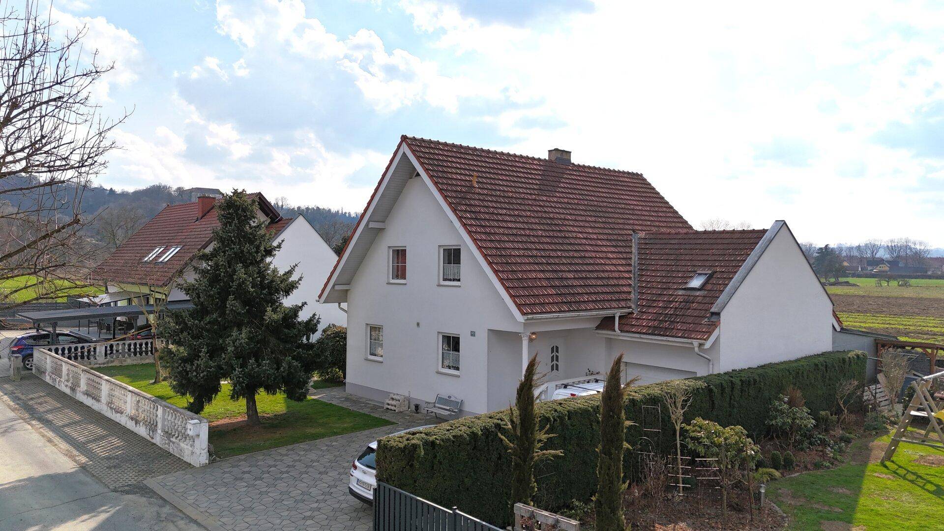 Einfamilienhaus mit rotem Ziegeldach, gepflasterter Einfahrt und grüner Hecke.