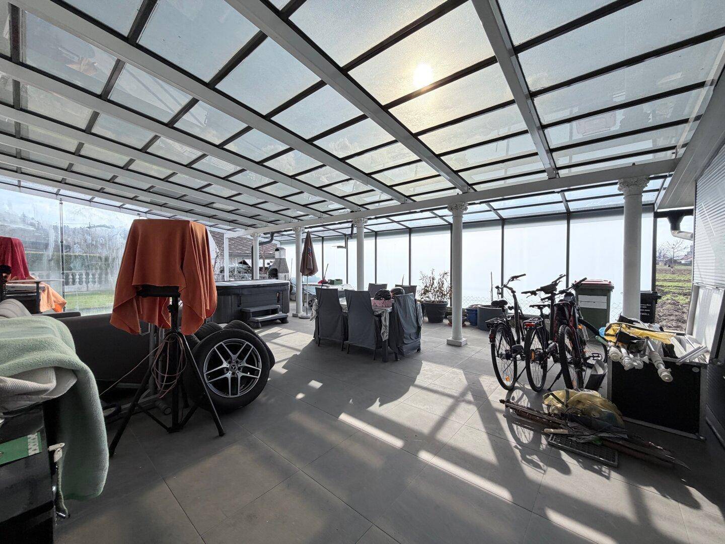 Große überdachte Terrasse mit Glasdach, Essbereich und Fahrrädern.