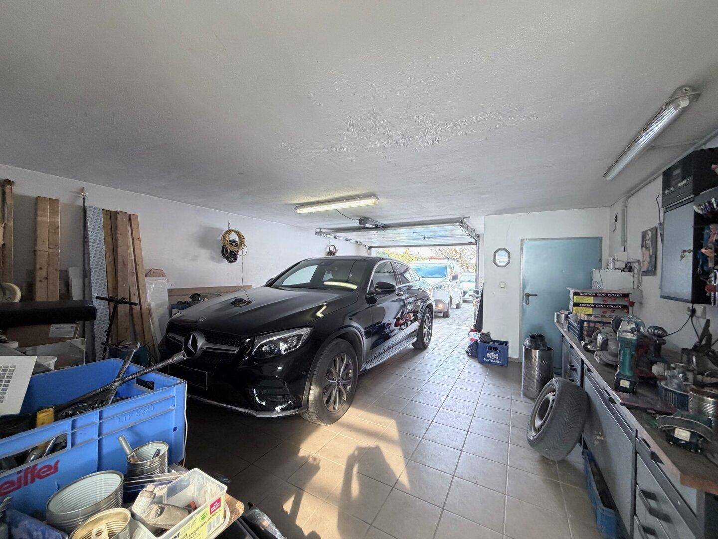 Geräumige Garage mit Fliesenboden und Platz für ein Fahrzeug sowie Werkstattbereich.