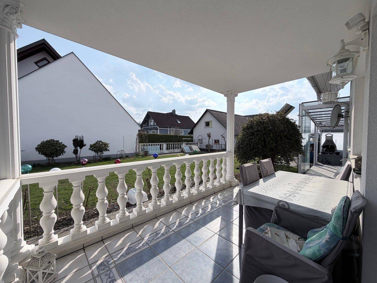 Überdachter Balkon mit Balustrade, Fliesenboden und Gartenmöbeln für entspannte Stunden.