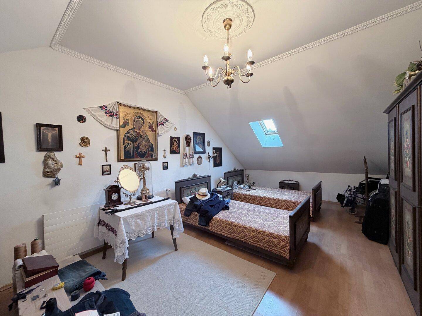 Schlafzimmer im Dachgeschoss mit zwei Einzelbetten, Dachfenster und Holzboden.