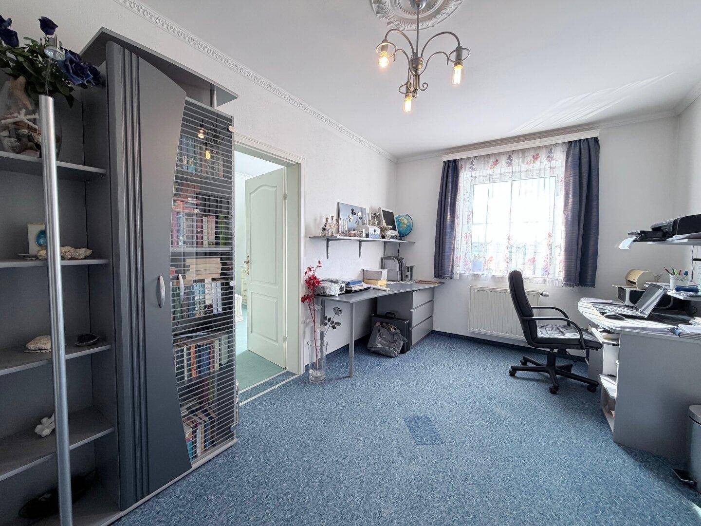 Arbeitszimmer mit blauem Teppichboden, Schreibtisch und Bücherregal.