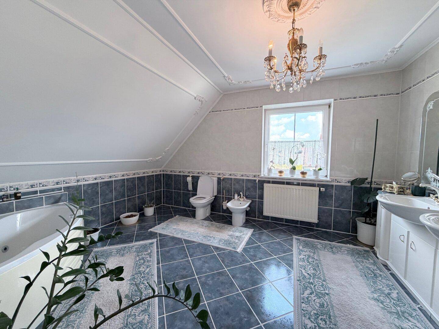Großes Badezimmer mit Badewanne, Bidet, Doppelwaschbecken und blaugrauen Fliesen.
