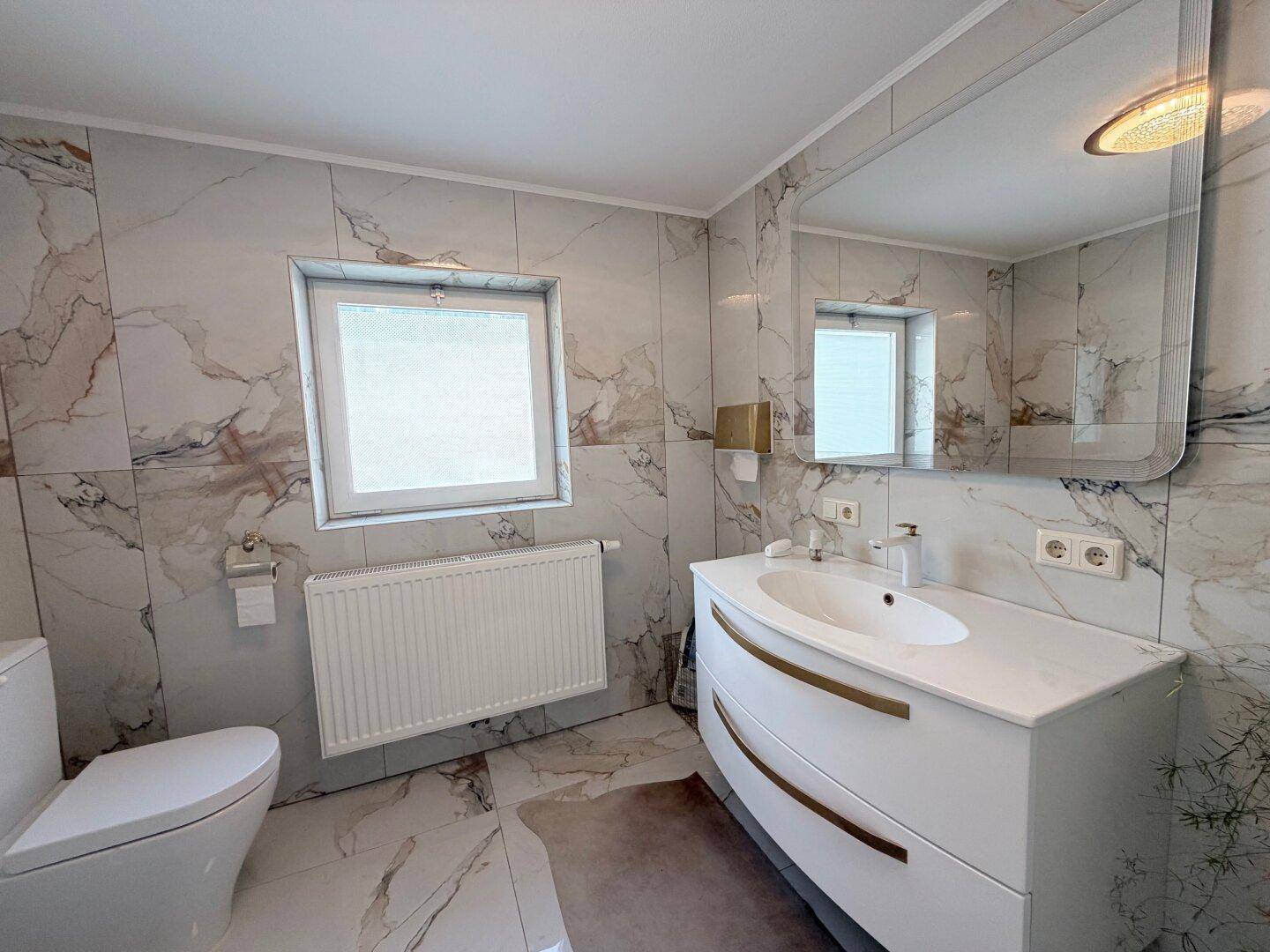 Modernes Badezimmer mit Marmorfliesen, Einzelwaschbecken und Fenster für Tageslicht.