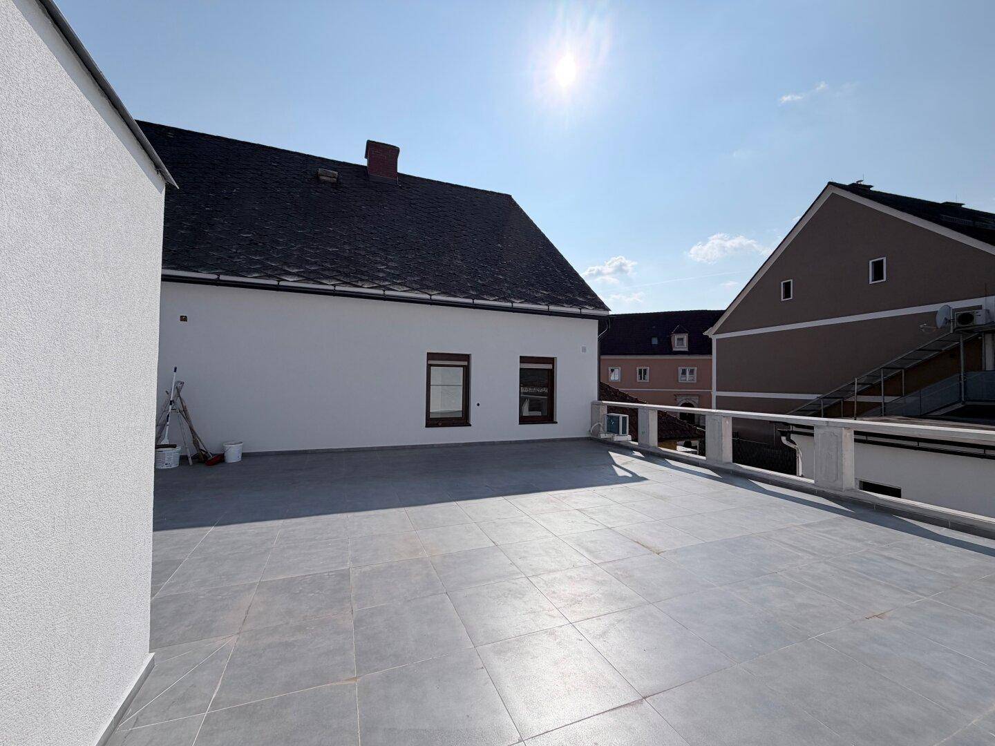 Große Dachterrasse mit grauen Fliesen und einer Brüstung, ideal für sonnige Tage.