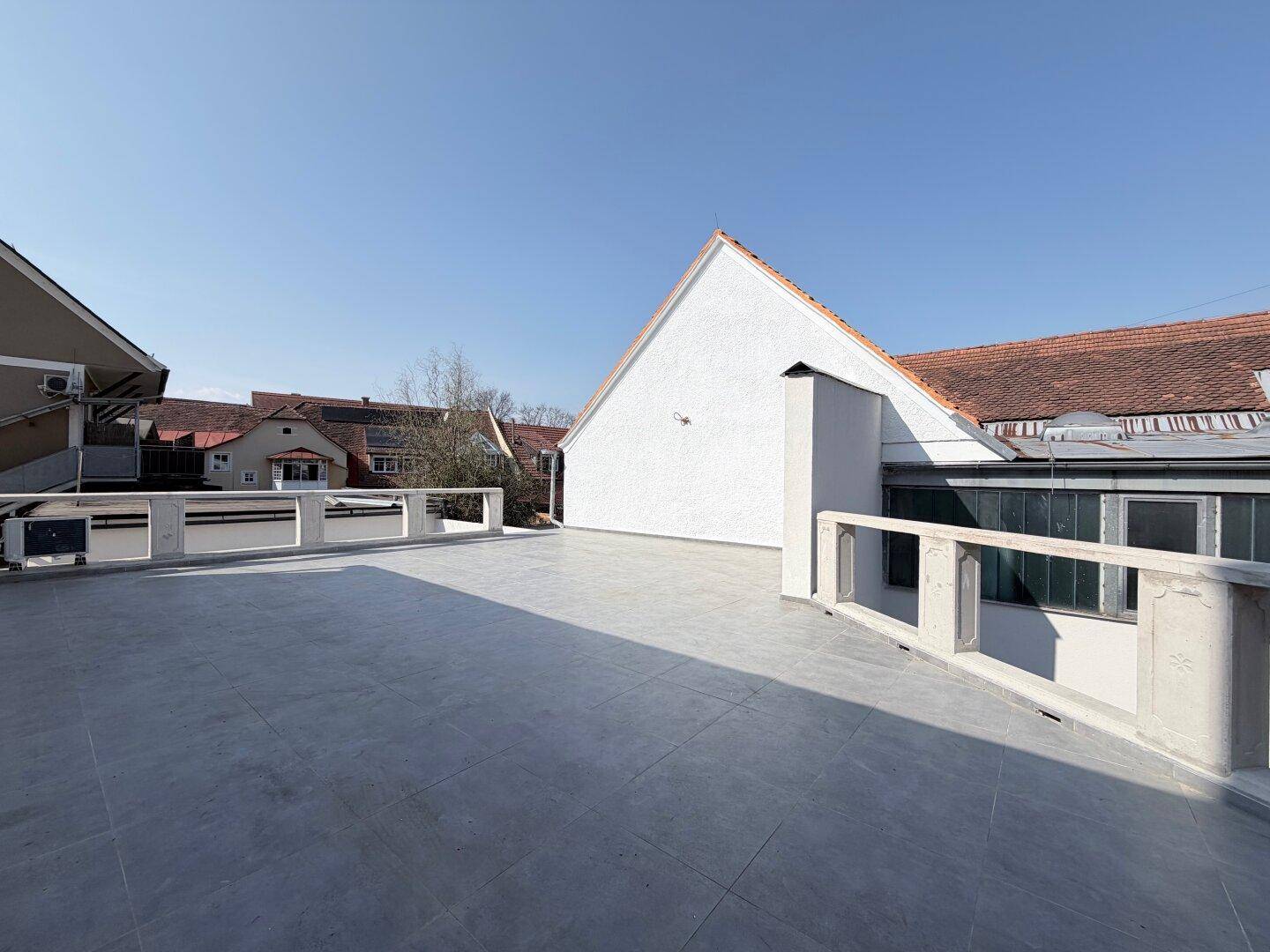 Weitläufige Dachterrasse mit grauen Fliesen und Blick auf die umliegenden Gebäude.