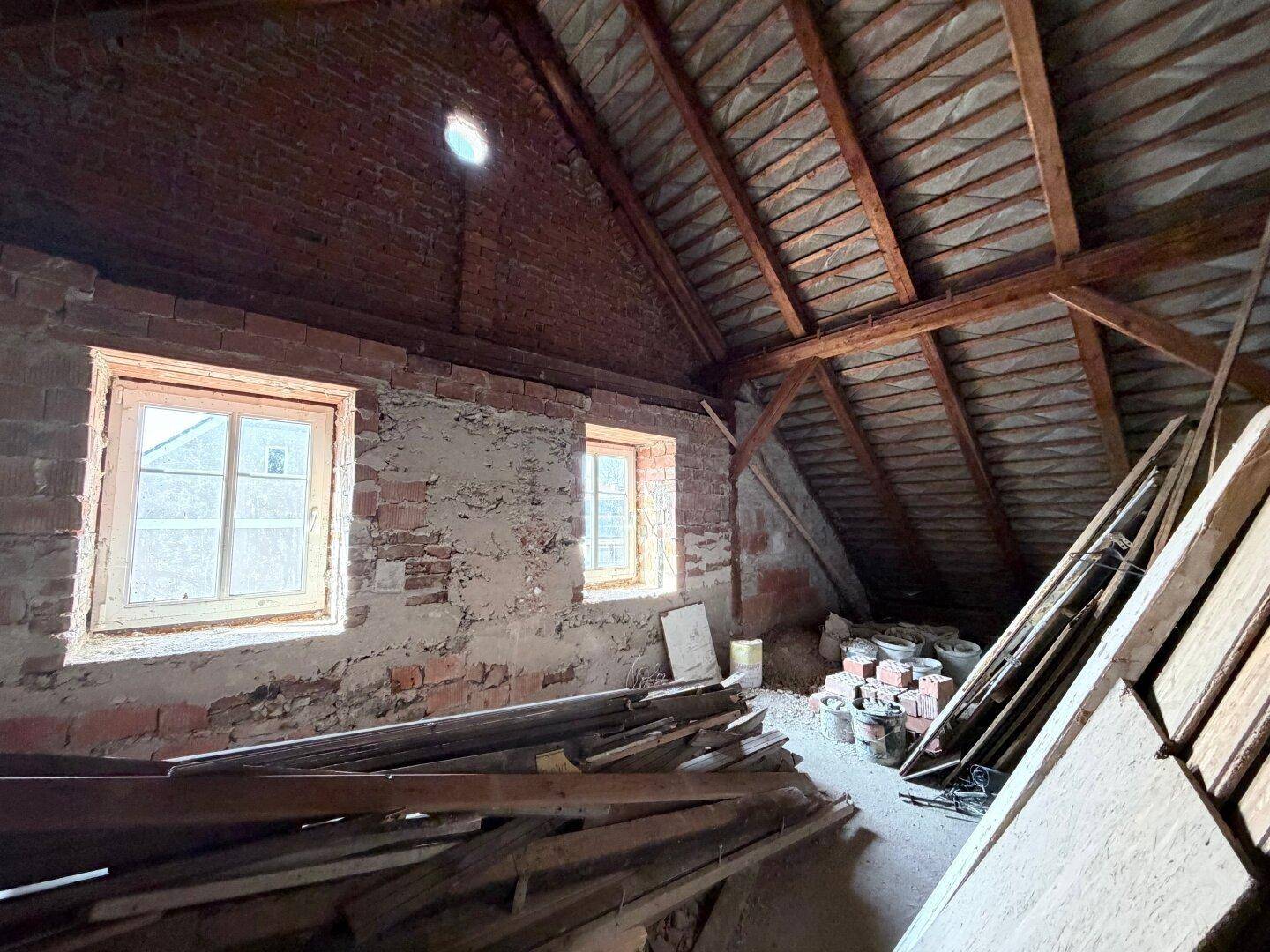 Unausgebauter Dachboden mit sichtbaren Ziegelwänden und Holzkonstruktion, bereit für den Ausbau.