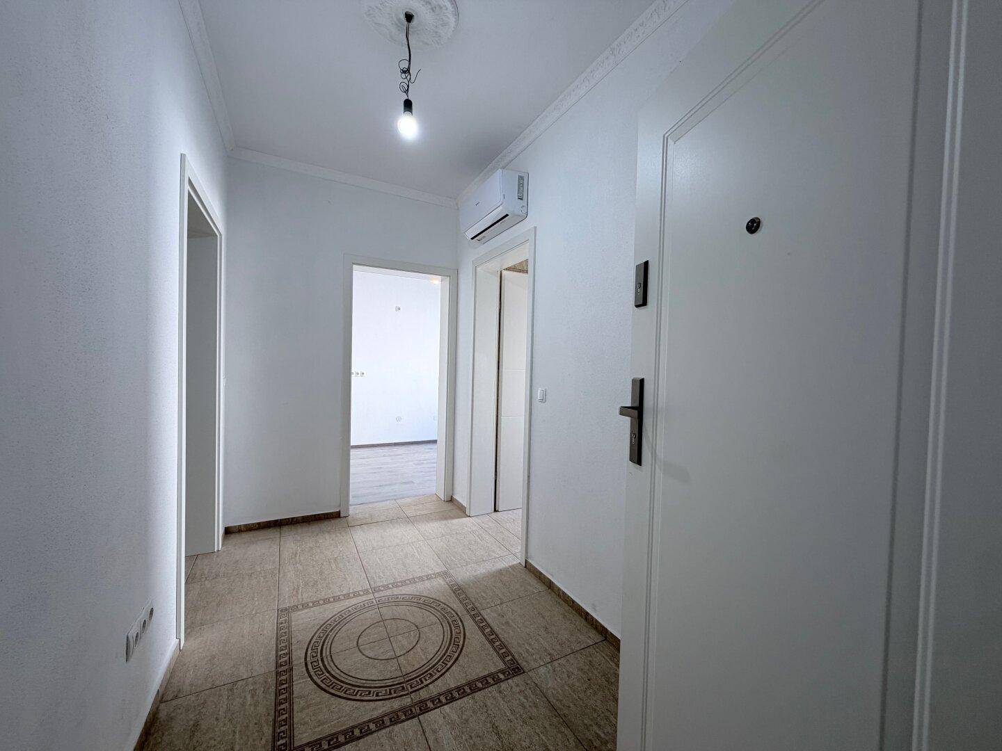 Heller Flur mit gemusterten Bodenfliesen und weißer Klimaanlage an der Wand.
