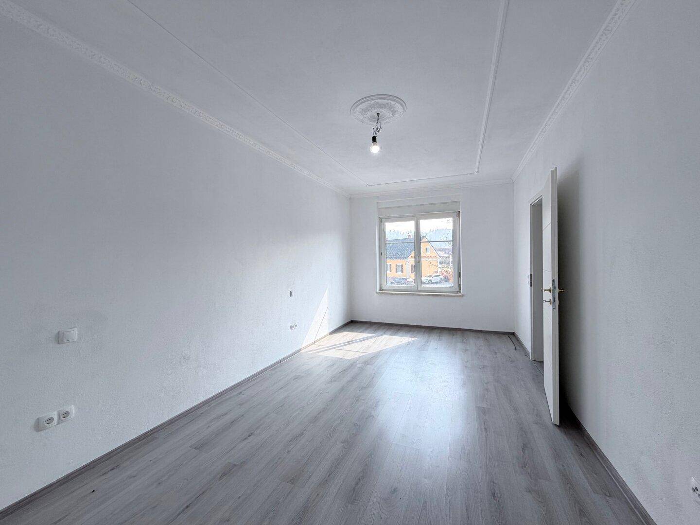 Leerer, heller Raum mit modernem Laminatboden und einem großen Fenster.