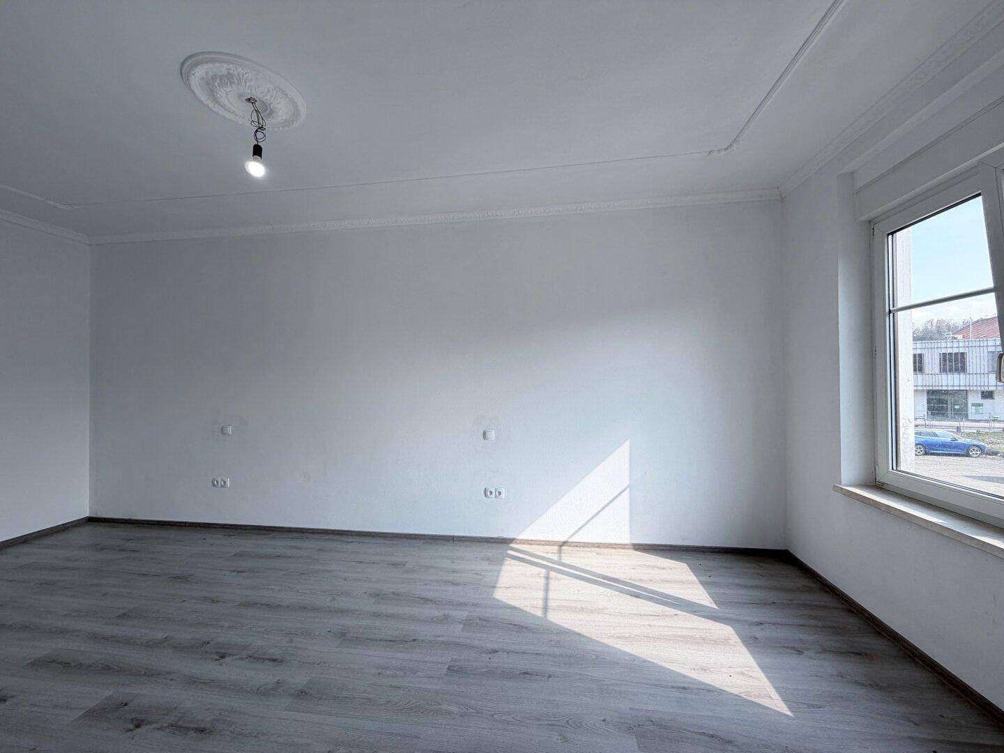 Geräumiger, leerer Raum mit hellem Laminatboden und viel Tageslicht durch das Fenster.