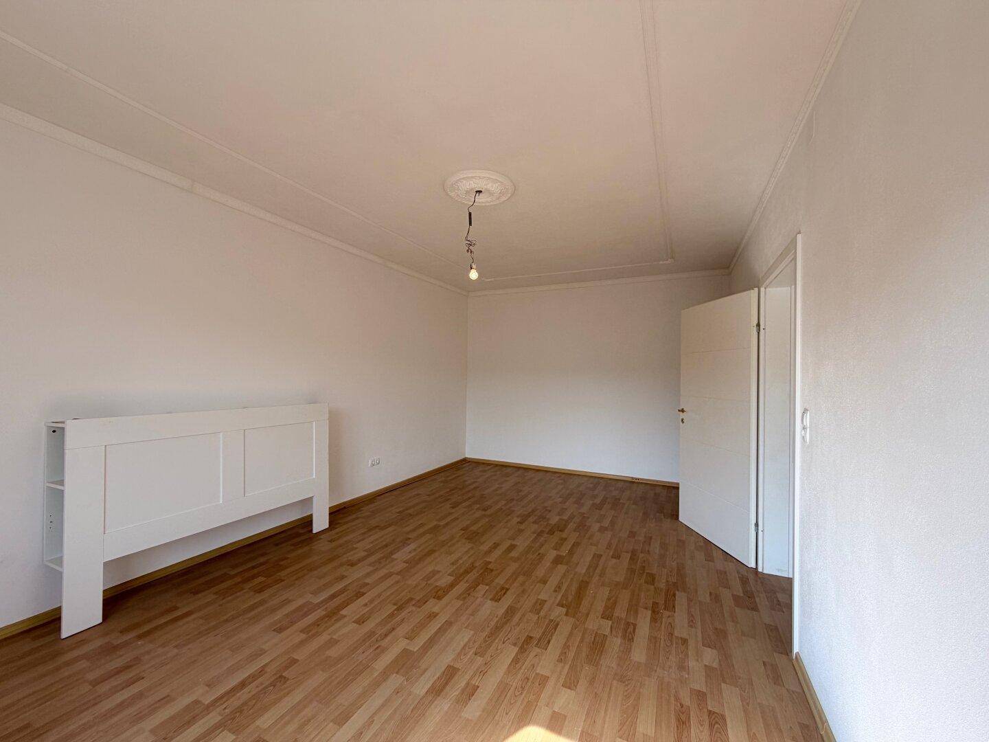 Leerer Raum mit hellem Holzlaminatboden und weiß gestrichenen Wänden.