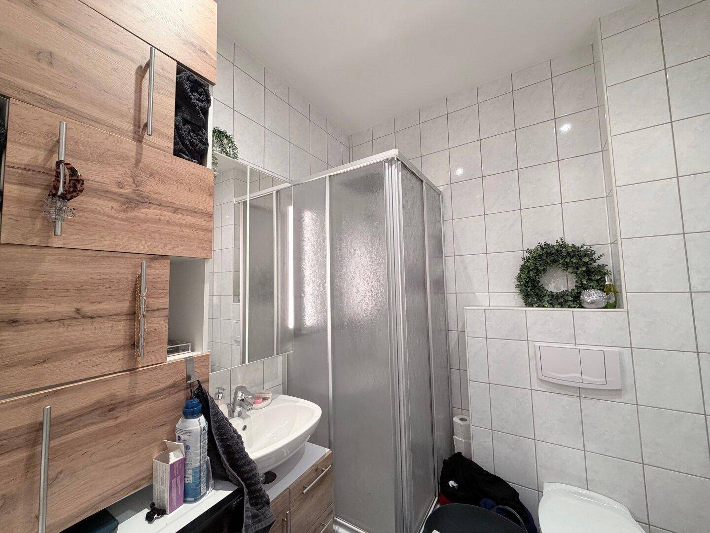 Kleines Badezimmer mit Duschkabine, Waschtisch und Holzschränken.