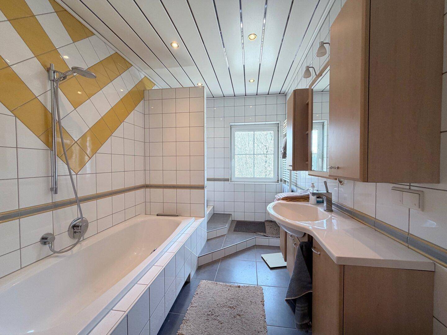 Badezimmer mit Badewanne, Waschtisch und gelb-weißen Fliesen im Dachgeschoss.