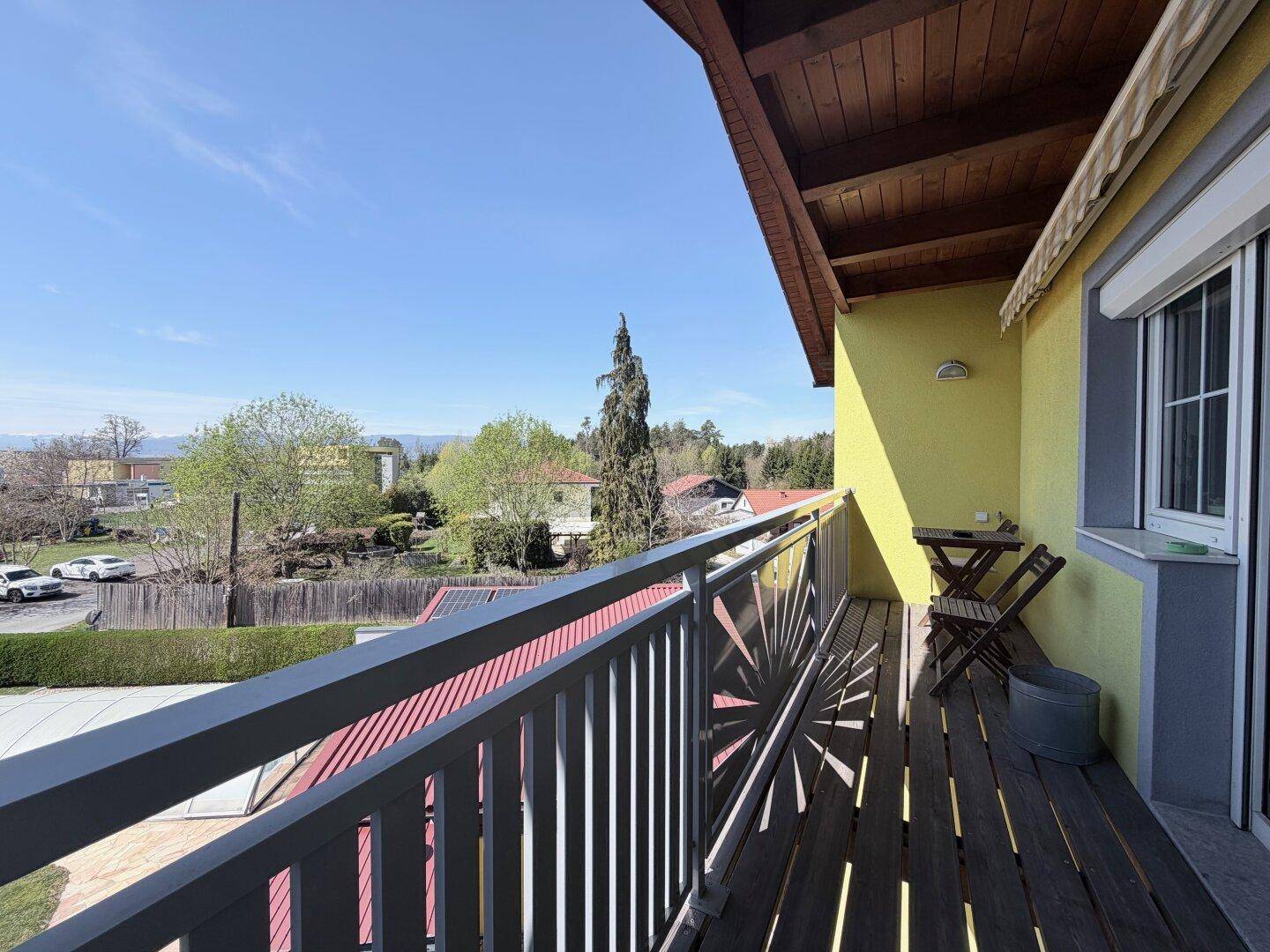 Sonniger Balkon mit Holzboden, Metallgeländer und Blick auf die Umgebung.