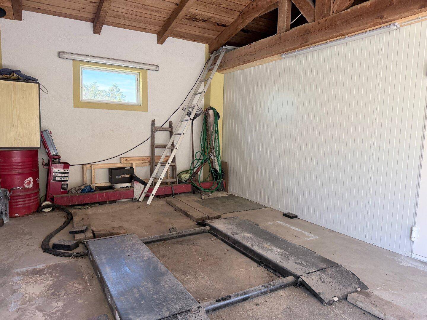 Werkstatt mit Hebebühne, Leiter und verschiedenen Geräten für Reparaturen.