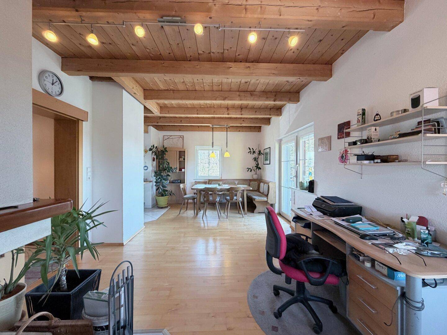 Heller Wohnbereich mit Holzbalkendecke, Parkettboden und integriertem Arbeitsplatz.