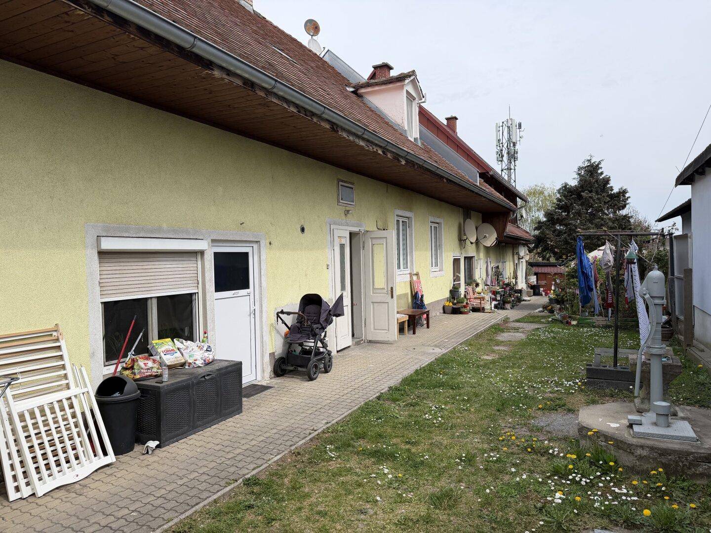 Seitenansicht des Gebäudes mit gelber Fassade, gepflastertem Weg, mehreren Eingängen und Wäscheleine.