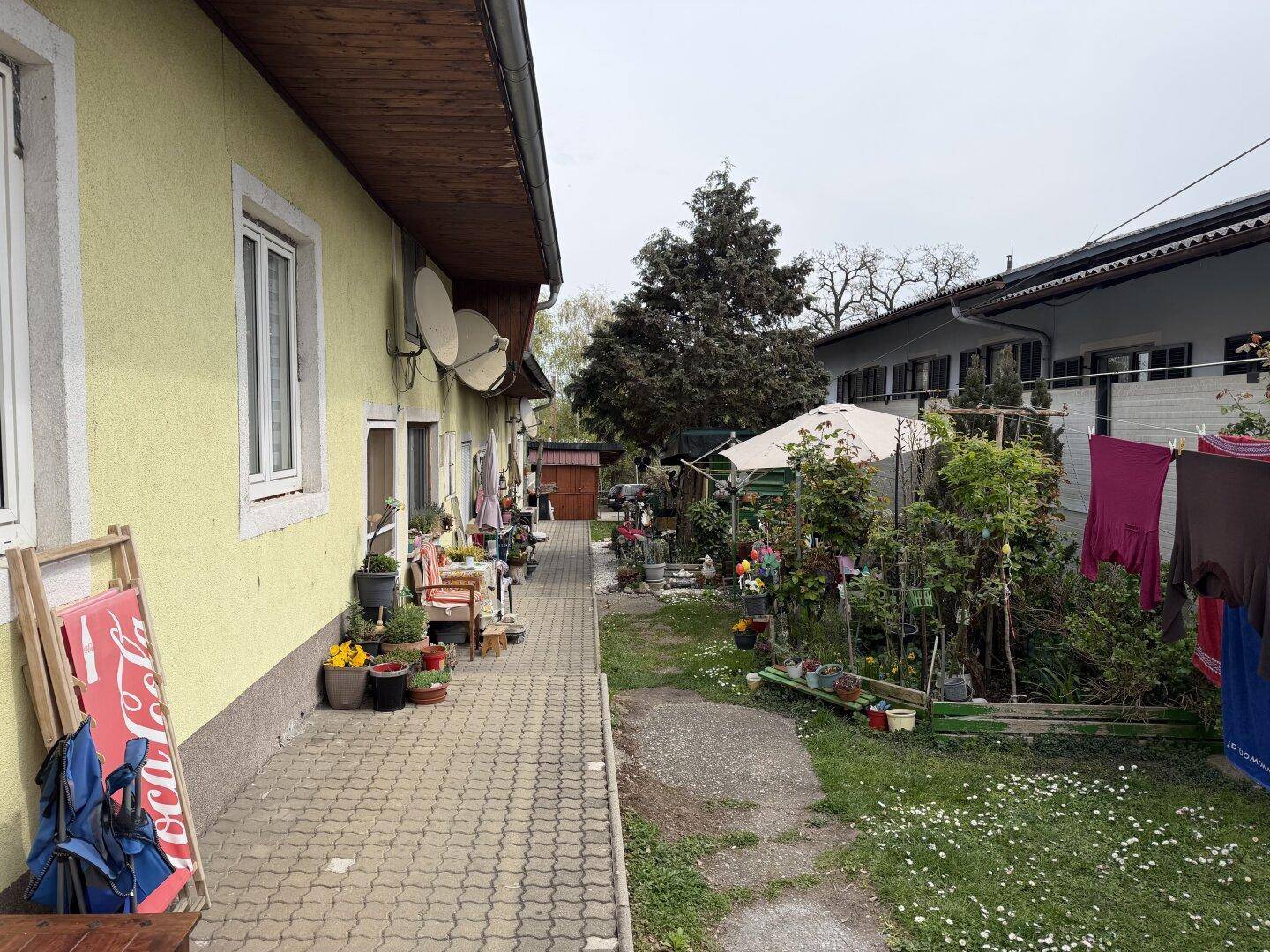 Gartenbereich entlang der Hausfassade mit vielen Pflanzen, Dekorationen und einer Wäscheleine.