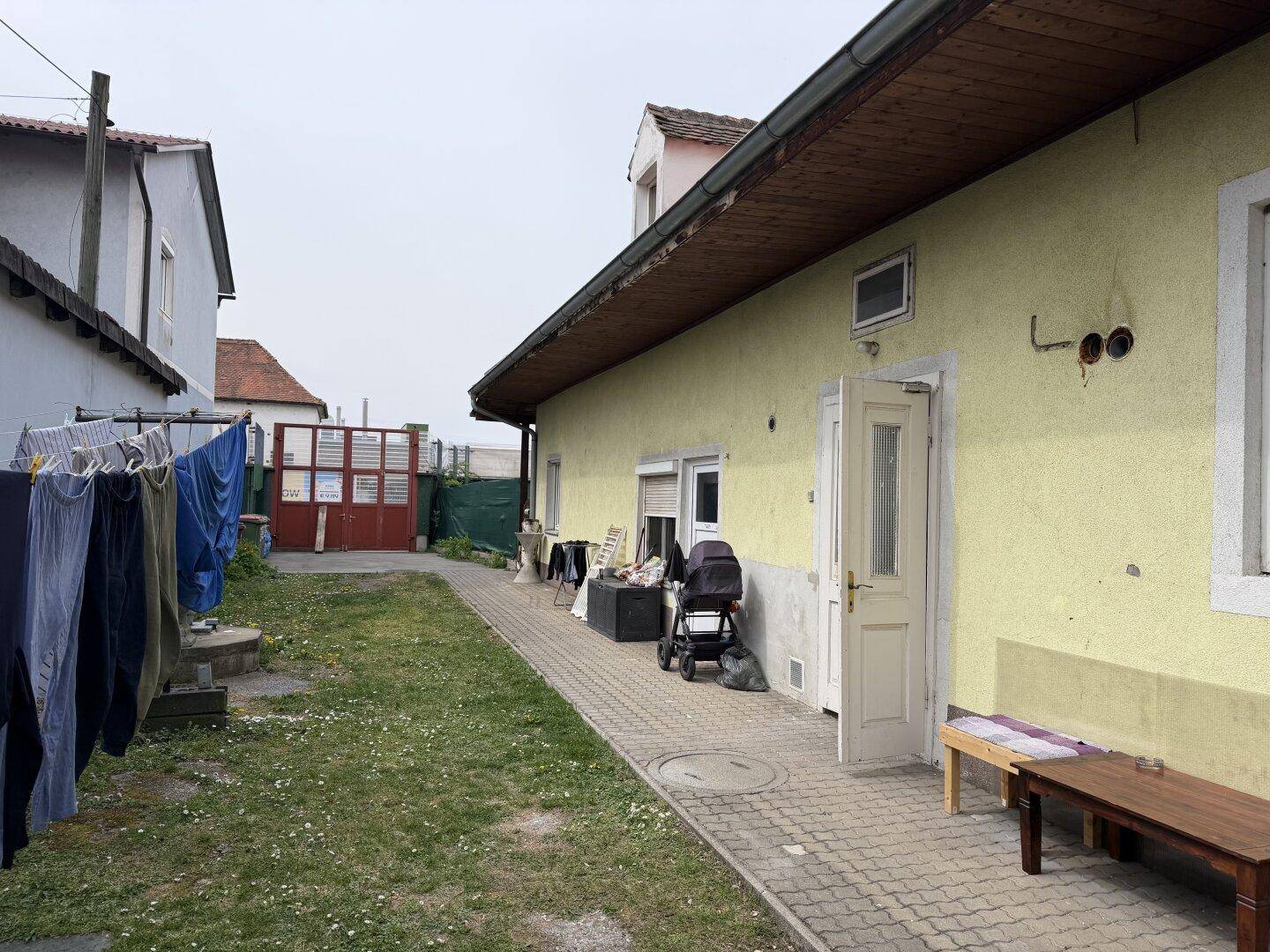 Rückansicht des Gebäudes mit Rasenfläche, gepflastertem Weg und Wäscheleine im Vordergrund.