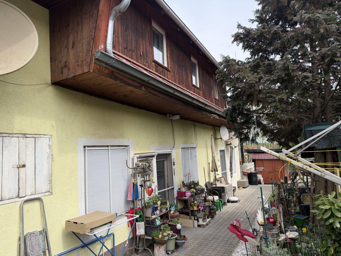 Seitenansicht des Hauses mit gelber Fassade im Erdgeschoss und Holzverkleidung im Obergeschoss.
