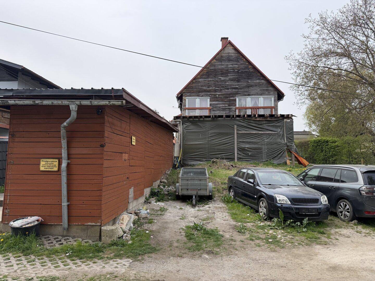 Rückseite des Grundstücks mit Holzschuppen, geparkten Autos und teilweise verdecktem Gebäude.