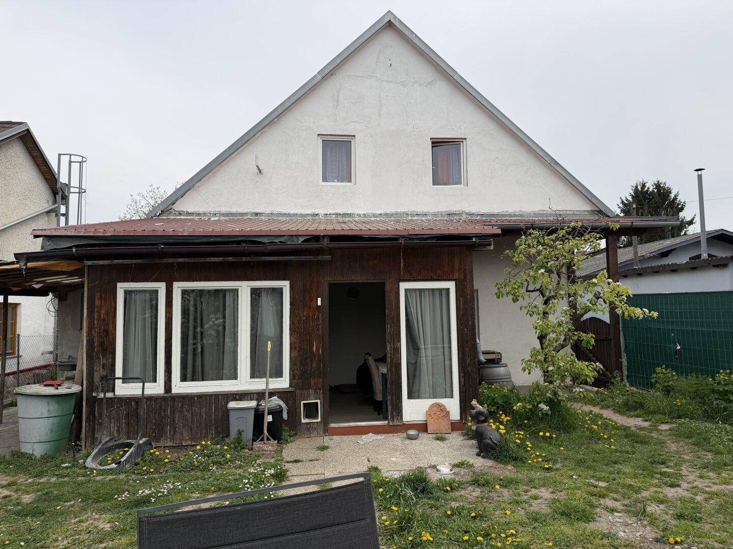 Rückseite des Hauses mit überdachtem Bereich, Gartenfläche und Giebeldach.