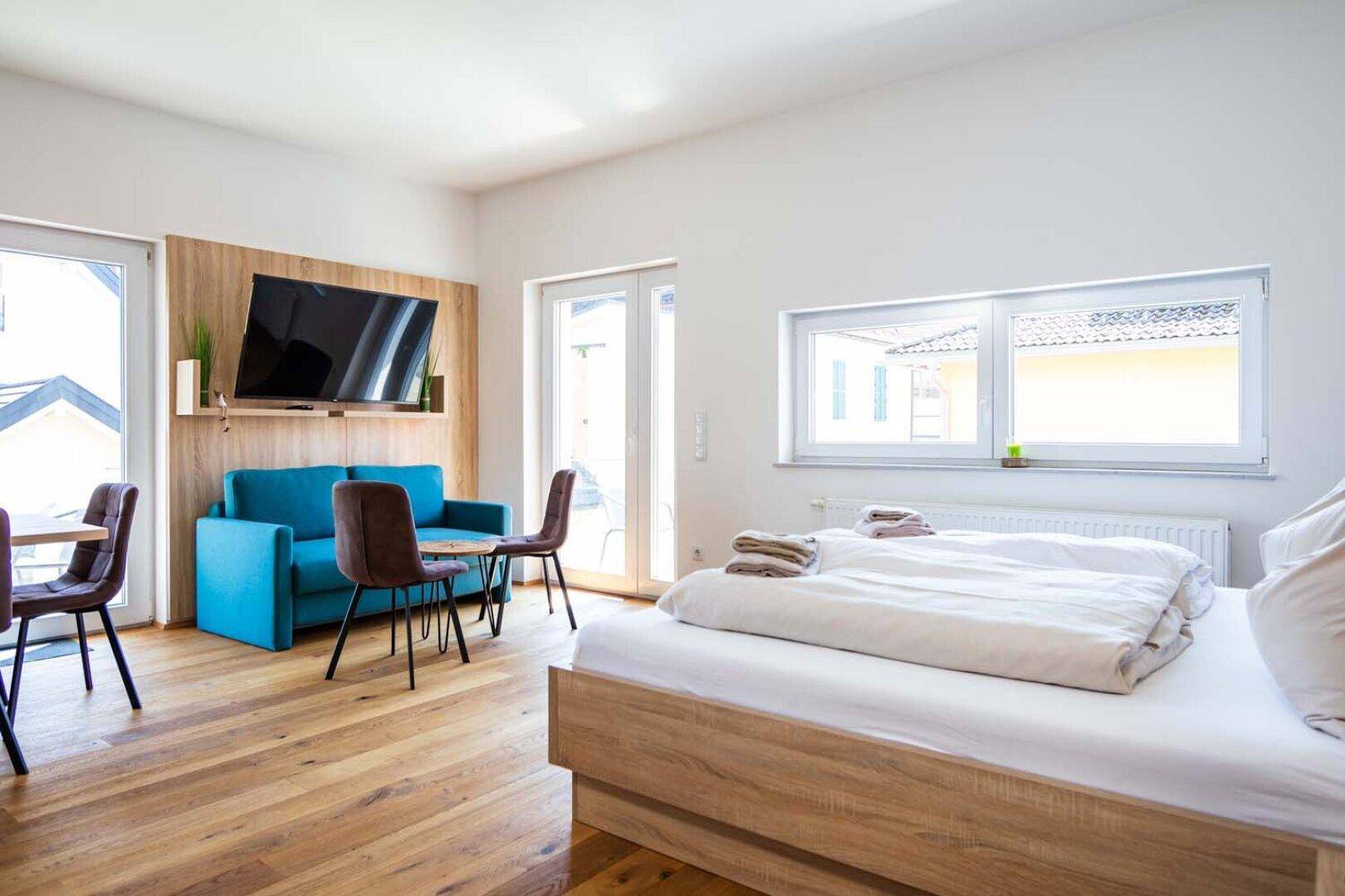 Modernes Schlafzimmer mit Holzboden, Doppelbett und einem kleinen Sofa, hell und freundlich.