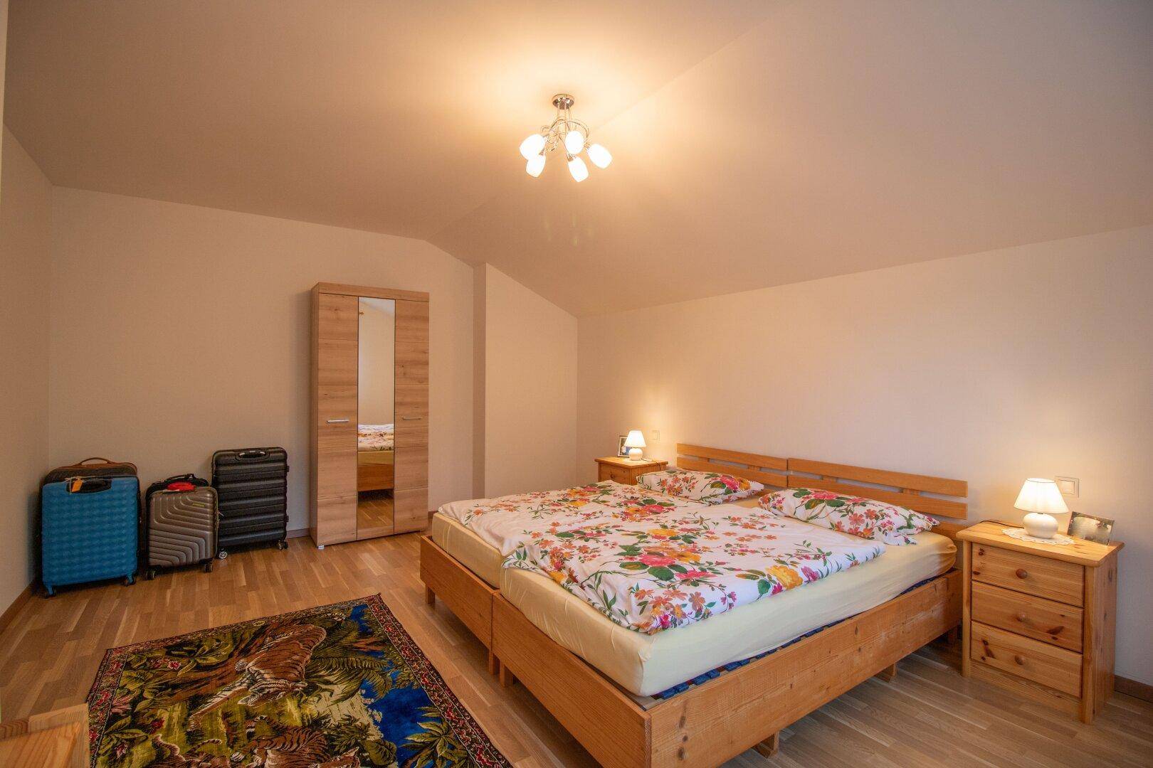 Schlafzimmer mit Doppelbett, Holzmöbeln und farbenfroher Bettwäsche.
