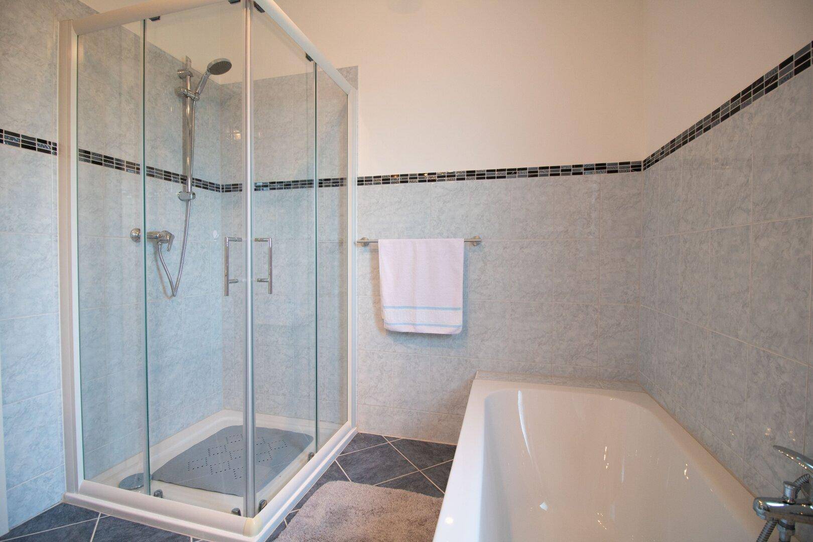 Modernes Badezimmer mit Duschkabine und Badewanne, hell gefliest.