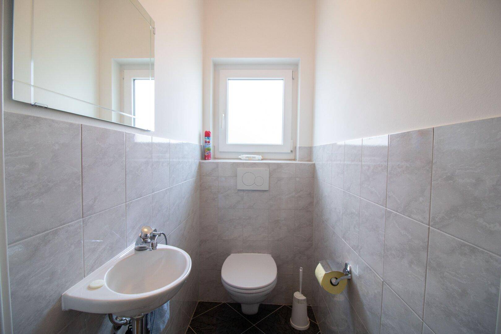 Separates Gäste-WC mit Wand-WC, Waschbecken und Fenster.