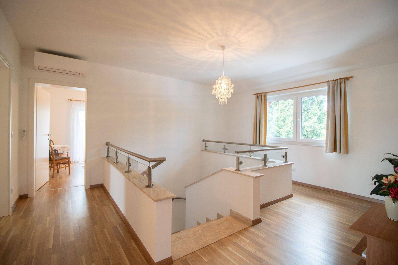 Geräumiger Flur mit Holzfußboden, Treppe und Fenster, das viel Licht hereinlässt.