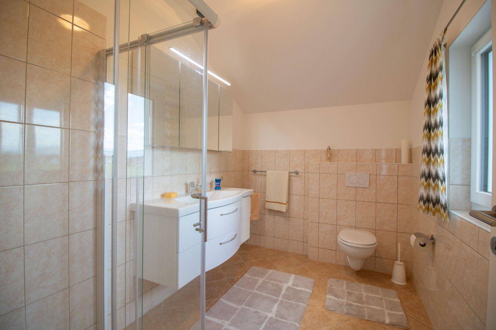 Badezimmer mit Duschkabine, Waschtisch, WC und beigefarbenen Fliesen.