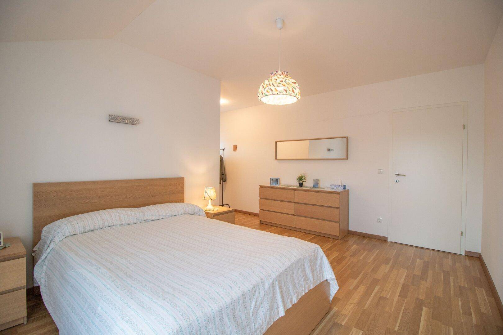 Schlafzimmer mit Doppelbett, Kommode und hellem Holzfußboden.