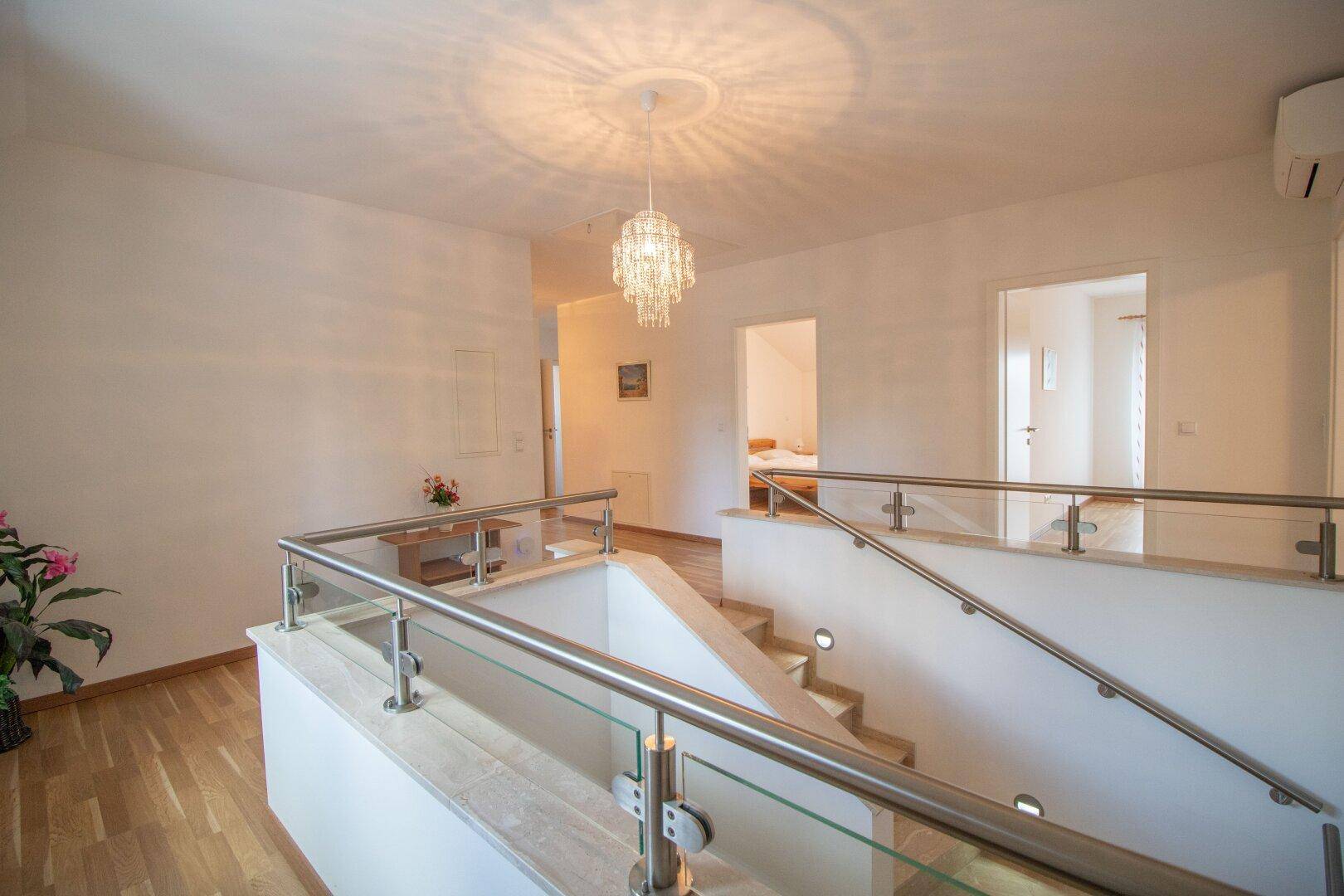 Heller Flur im Obergeschoss mit Holzparkett und moderner Glasgeländer-Treppe.
