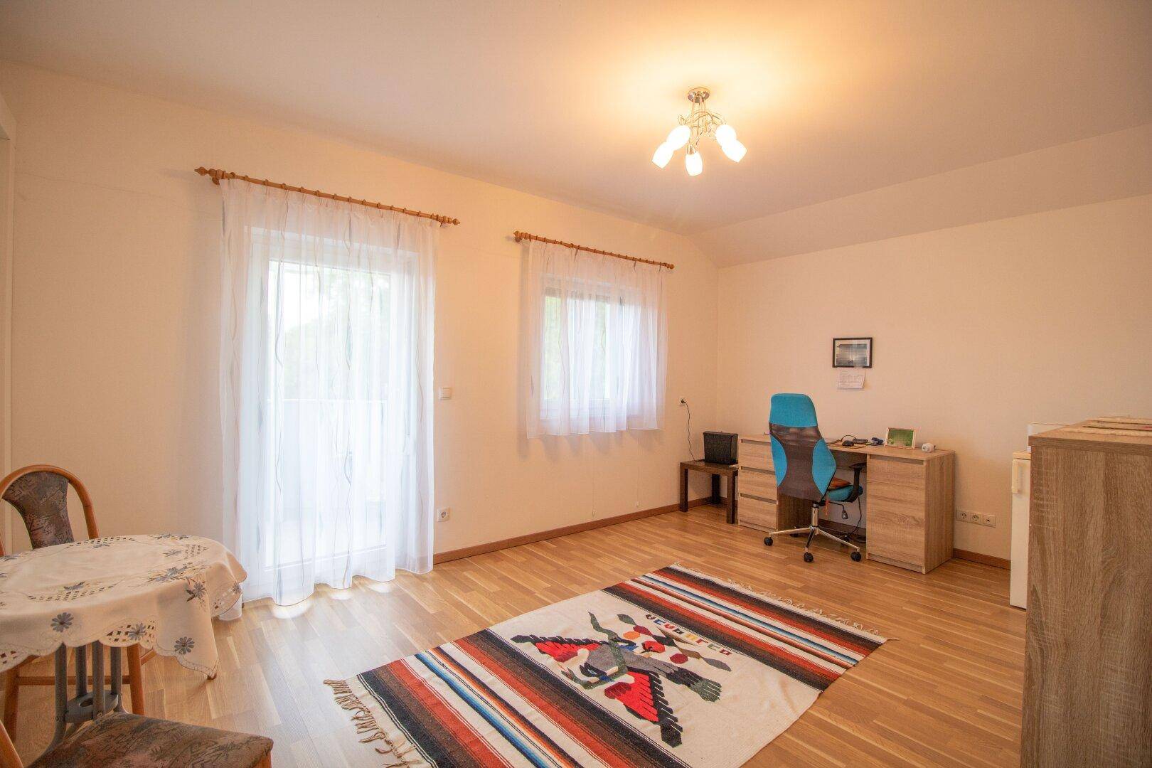 Helles Zimmer mit Schreibtisch, Stuhl und Teppich auf Holzfußboden.