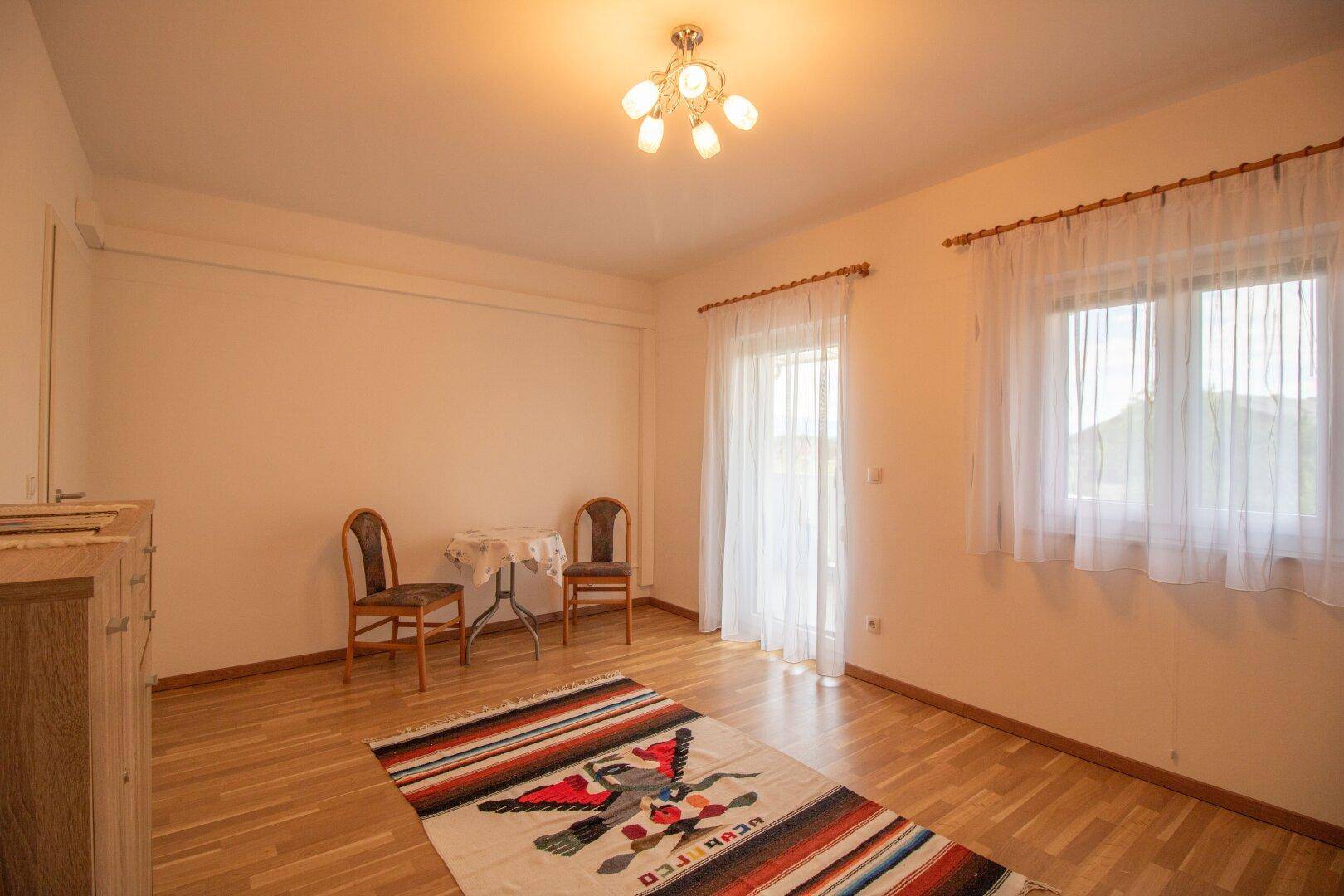 Heller Raum mit zwei Stühlen, kleinem Tisch und Teppich auf Holzfußboden.