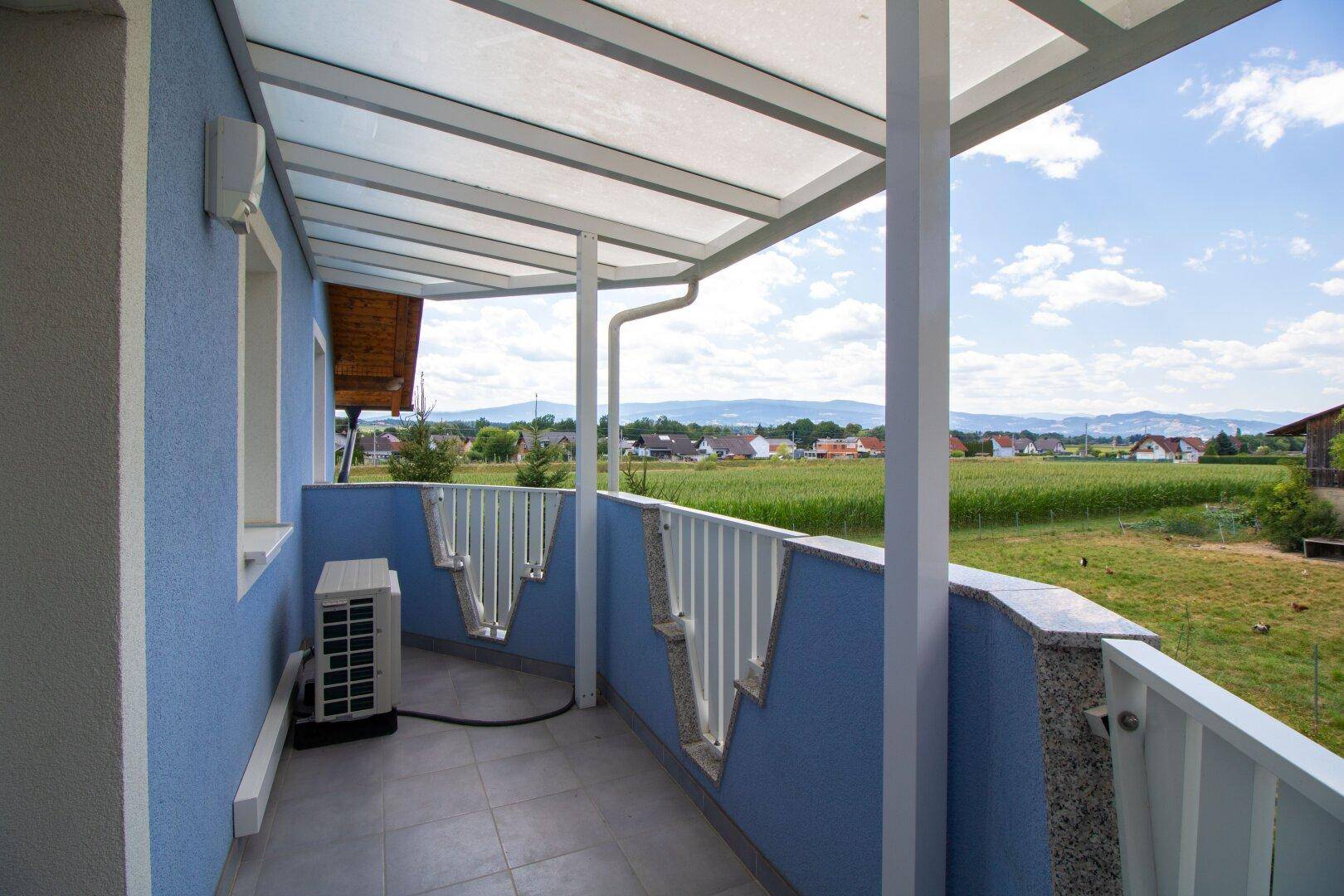 Überdachter Balkon mit Fliesenboden und Blick auf die grüne Landschaft.