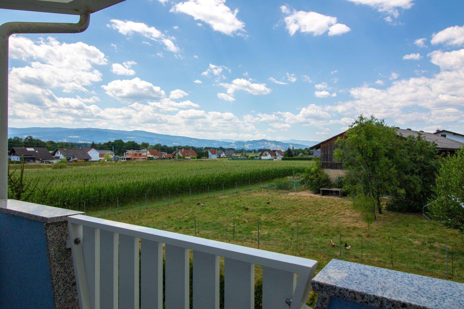 Weitläufiger Blick über grüne Felder und ländliche Umgebung mit Bergen am Horizont.