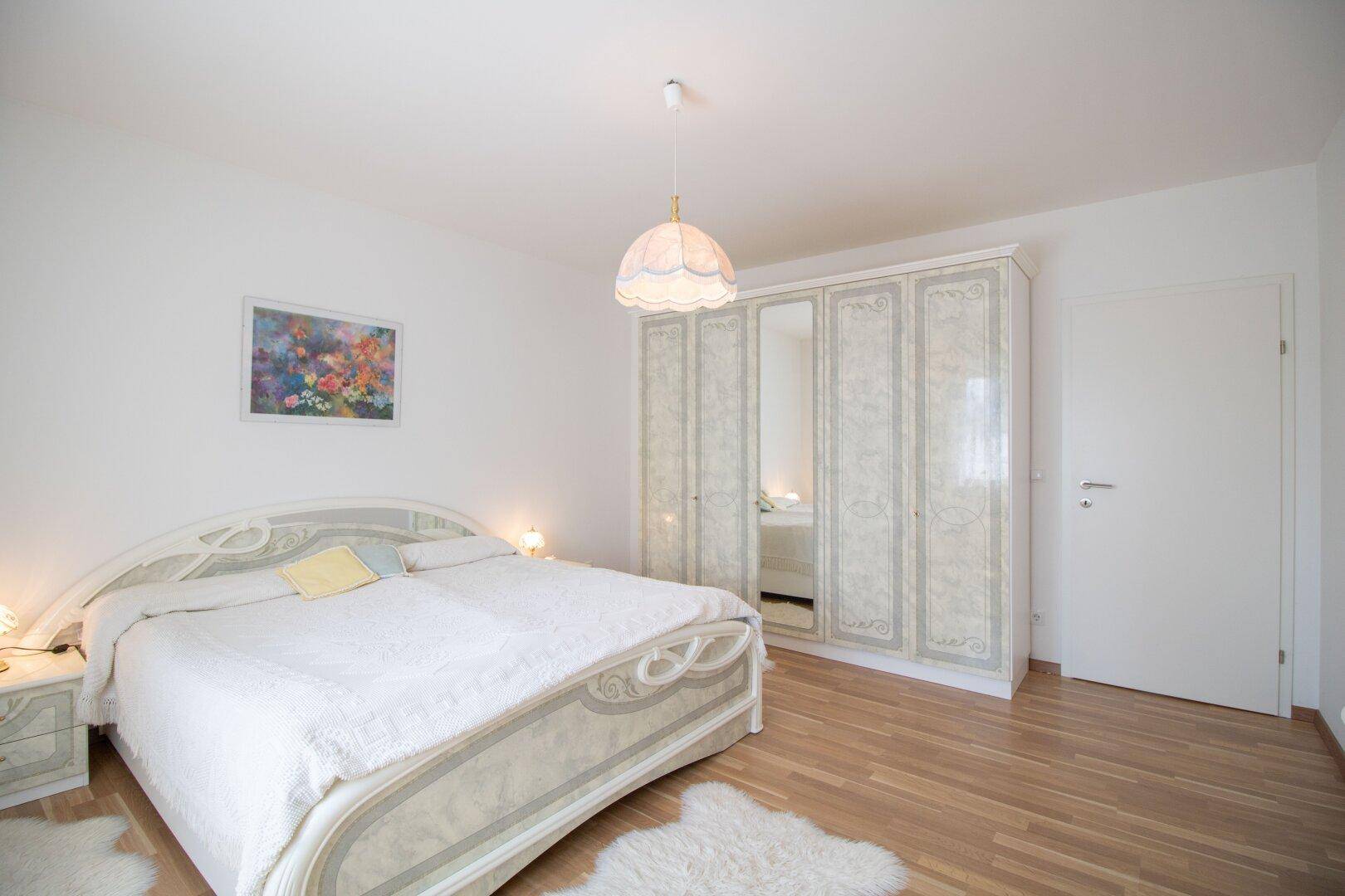 Helles Schlafzimmer mit großem Kleiderschrank, Doppelbett und Parkettboden.