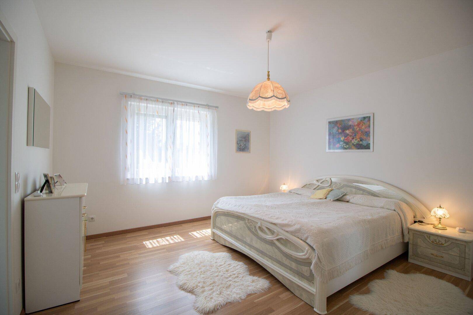 Gemütliches Schlafzimmer mit Doppelbett, Parkettboden und Fenster mit Vorhängen.