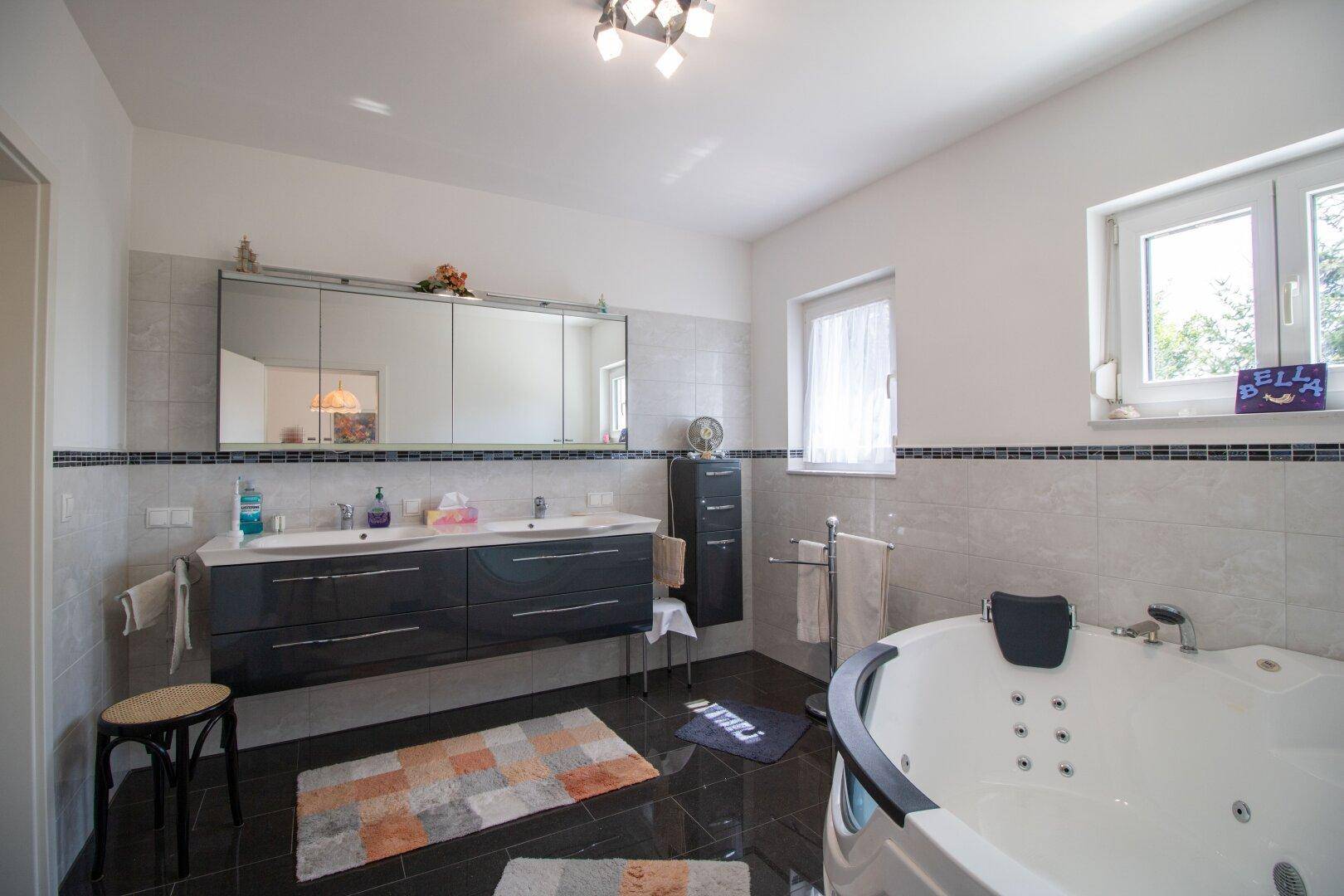 Modernes Badezimmer mit Doppelwaschbecken, Whirlpool-Badewanne und Fenster.