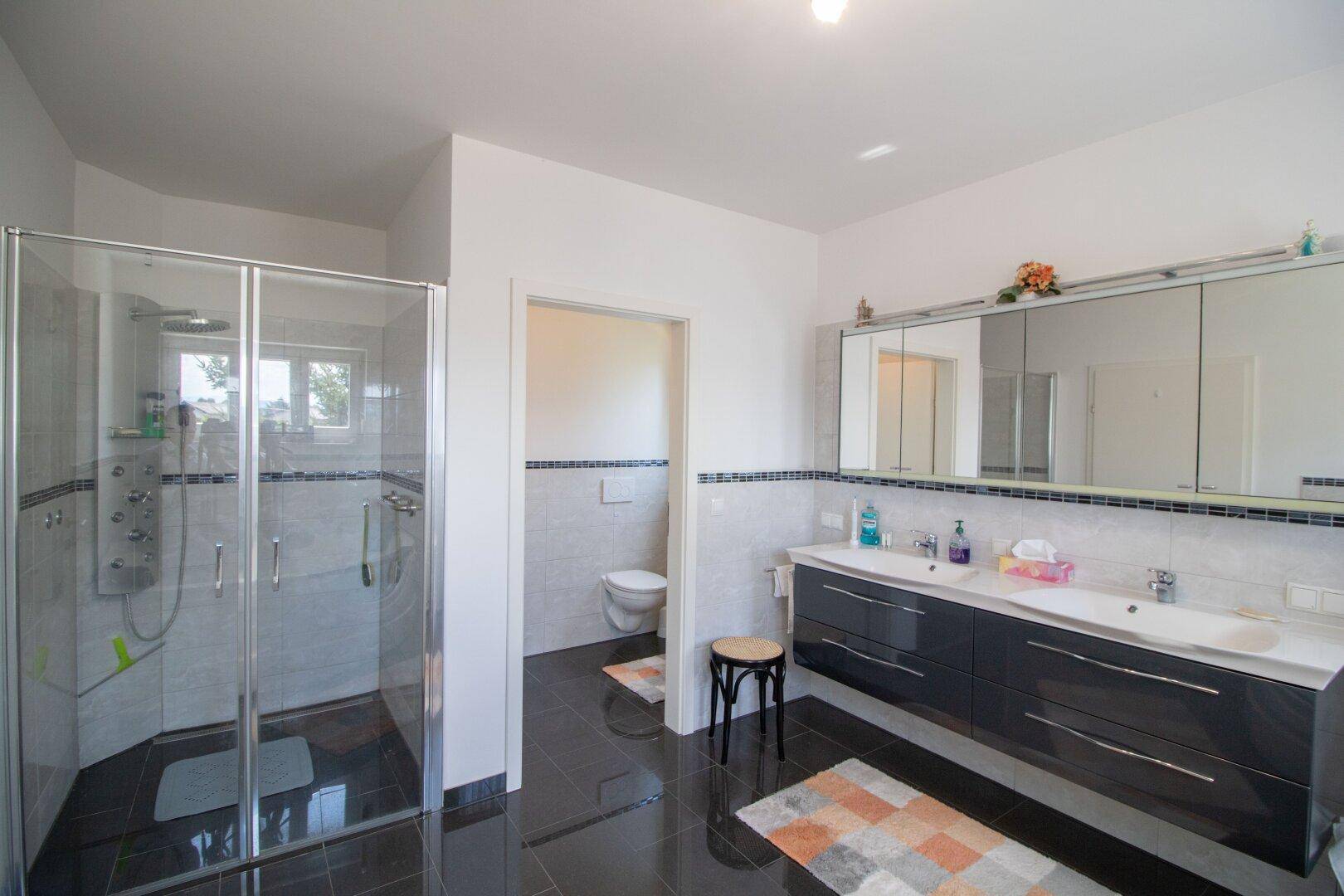 Modernes Badezimmer mit Duschkabine, Doppelwaschbecken und separatem WC-Bereich.
